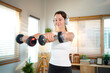 © Stella 16 - Athletic woman lifting dumbbells and listening to music with headphones during home workout