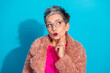 © deagreez - Curious stylish mature woman with pink fur coat and glasses poses against blue background thinking mode playful fashion wellness and lifestyle advertising