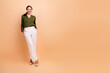© deagreez - Young woman posing in green blouse and white pants against a peach background smiling confidently in fashion style