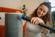 © wifesun - Woman cleaning an air purifier filter at home using a vacuum cleaner attachment, carefully removing accumulated dust to maintain the device and improve indoor air quality