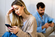 © NDABCREATIVITY - Young couple sitting back to back, both focused on their smartphones, appearing emotionally distant
