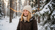 © tonstock - Happy woman wearing warm clothes enjoys a winter vacation in a snowy forest with glowing lights.