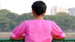 © Mary_muis/stoker ua - Woman in pink blouse standing at railing, gazing into the distance with a lush green landscape and urban buildings visible in the background