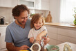 © Stockphotodirectors - A father and his young child share joyful moments while preparing ingredients in a bright kitchen, creating special memories during their time together.