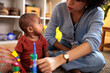© Jovo Jovanovic/Stocksy - Baby looks up at caregiver playing with stacking toy.