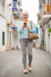 © Paula - Happy senior woman listening to music while walking in city