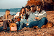 © ivanko80 - Friends gather by the water at sunset for music and a picnic with a guitar, smiles, and good company