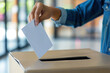 © ExF Designs - Close up of voter hand wearing blue denim jacket inserting ballot paper into cardboard election box