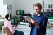 © Mediaphotos - Young man using digital tablet in office while Black young man working at computer in background, both focused on technology tasks in workspace
