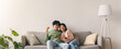 © Prostock-studio - Two people sit closely on a couch in a living room. They look at a tablet together while one holds a credit card. Sunlight streams in from a window, creating a warm space.