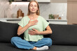 © brizmaker - Woman engages in mindfulness practice at home while sitting on the couch