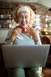 © Geber86 - Smiling senior woman with facial mask using laptop at home