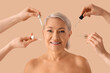 © Pixel-Shot - Mature woman and female hands with collagen serums on beige background