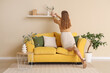 © Pixel-Shot - Young woman putting vase with eucalyptus branches on shelf in room. Back view