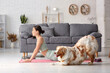© Pixel-Shot - Young woman with Australian Shepherd dog stretching in living room