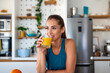 © Graphicroyalty - Beautiful woman in athletic wear drinks fresh orange juice from a glass in a bright kitchen. High-quality lifestyle image focusing on healthy nutrition, morning routines, and wellness for commercial.