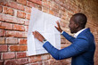 © Westend61 - Smiling businessman studying plan at brick wall