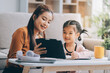 © ARMMY PICCA - A cheerful Asian mother helps her young daughter do homework and color a book at home, while the father works on a laptop in the background. A cozy, bright, and modern family lifestyle.