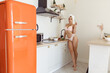 © Vlad - Young beautiful female in pink lingerie with towel on head after shower posing in kitchen while cooking breakfast. Pretty woman in underwear preparing food indoors. Morning concept