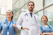 © StockMe - Confident healthcare professionals smiling, standing outside a modern hospital building, ready to provide healthcare services and support