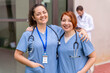 © StockMe - Healthcare team smiling, two happy nurses wearing scrubs and stethoscopes working at hospital, male doctor in background