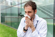 © StockMe - Medical professional feeling unwell, sneezing and blowing nose into a tissue, experiencing illness symptoms outdoors