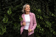 © Westend61 - Smiling woman in pink jacket enjoying outdoor park with greenery