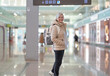 © luciano - Smiling senior caucasian traveler woman with backpack at the airport gate waiting for departure flight, elderly woman looking at camera
