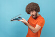 © khosrork - Portrait of curious man with Afro hairstyle wearing orange T-shirt taking a look at laptop display, trying to see private information, spying. Indoor studio shot isolated on blue background.