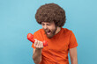 © khosrork - Portrait of angry man with Afro hairstyle wearing orange T-shirt screaming and yelling talking retro landline phone, complaining on connection quality. Indoor studio shot isolated on blue background.