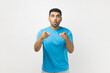 © khosrork - Portrait of excited amazed astonished unshaven man wearing blue T- shirt standing pointing index fingers to camera, expressing astonishment. Indoor studio shot isolated on gray background.