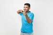 © khosrork - Portrait of positive delighted satisfied unshaven man wearing blue T- shirt standing pointing index fingers at camera, choosing you. Indoor studio shot isolated on gray background.