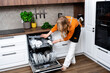 © 5ph - Woman organizing glass cups in upper rack of dishwasher. Careful handling of fragile kitchenware with modern electronic cleaning equipment.