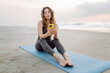 © maxbelchenko - Woman on blue mat with phone and wireless headphones against backdrop of sea. Athletic woman listens to music and enjoys sunrise against backdrop of seascape. Concept of meditation and relaxation.