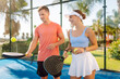 © maxbelchenko - A young man and woman play padel together on a sunny day. Cheerful friends with rackets and balls on a padel court. Concepts of play, sport, and fun.