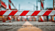 © Mikhail Vorobev - Red and white striped barrier blocking a road under construction with blurred equipment and pavement detail in a close-up urban worksite scene