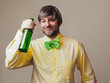 © mark_gusev - Excited man in his 40s or 50s in a yellow shirt and Irish green bow tie with shamrock is holding a bottle of beer. Light color background. Ireland sport fan. Male with grey beard and hair.