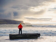 © mark_gusev - Tourist in red jacket is standing on a small rock with spectacular nature scenery with cliff, ocean and dramatic sky in the background. Doolin, area, Ireland. Travel and tourism.