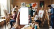 © Olga Ко - Female hand holding smartphone with blank screen in art studio with painters in background.