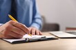 © New Africa - Man writing in clipboard with pen at wooden desk indoors, closeup