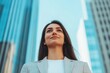 © Arfa_Media - Businesswoman looking up with determination and ambition towards a bright future, standing empowered against the backdrop of modern skyscrapers and urban architecture