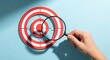 © fadillah - Hand holding magnifying glass over a red and white target on a blue background.