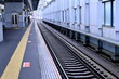 © taka - 駅のホームと線路、安全を支える黄色の点字ブロックが続く風景（公共交通機関・バリアフリー）