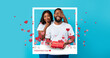 © Prostock-studio - A couple smiles and enjoys a moment together on Valentine's Day. The woman covers the man's eyes while he holds a red gift. They stand in front of a bright blue background.
