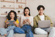 © Prostock-studio - Smiling teen child and young asian mother and father surfing in internet, chatting on gadgets, play game and searching offer, sit on sofa in living room interior. New normal, relax together at home
