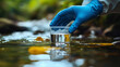 © Martinesku - Gloved hand taking a water sample from a contaminated river for laboratory testing. Concept of industrial pollution, environmental monitoring, and inspection control.
