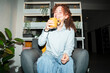 © Studio Marmellata - A young woman with curly hair laughs while drinking from a mug, seated comfortably in an armchair in a modern living space.