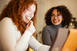 © Studio Marmellata - Two young women share a moment of laughter while looking at a screen, their faces illuminated by its glow.
