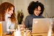 © Studio Marmellata - Two young women with curly hair are smiling and working together on a laptop in a casual setting.