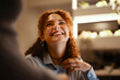 © Studio Marmellata - A young woman with curly hair laughs heartily while looking up at someone. Her eyes are closed in joy, and her hand is raised to her chest.
